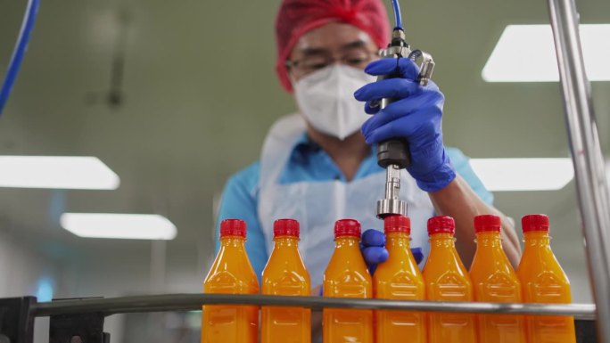 亚裔华裔男性果汁厂工人在生产线上封橙汁瓶盖