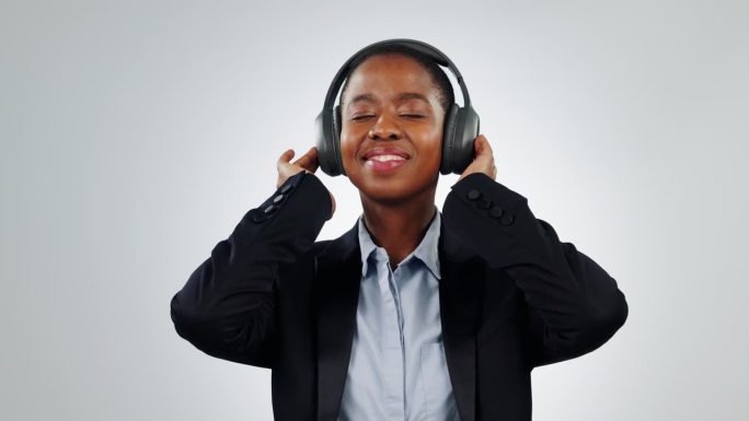 黑人女性，商务人士，戴着耳机跟着音乐跳舞，在录音室里听广播，背景是白色的。公司员工享受能量、锐舞或科