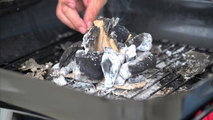 慢动作特写，一个男人的手用一根火柴点燃一块纸板，用烧过的木炭开始烧烤