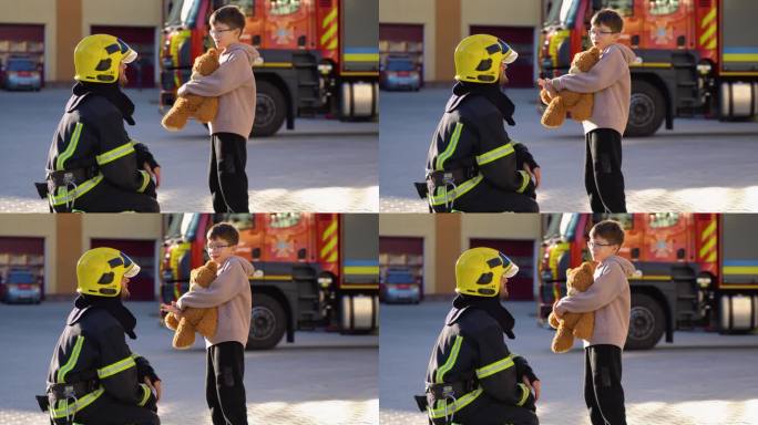 在消防站，小男孩拿着玩具和穿着防护服的消防员