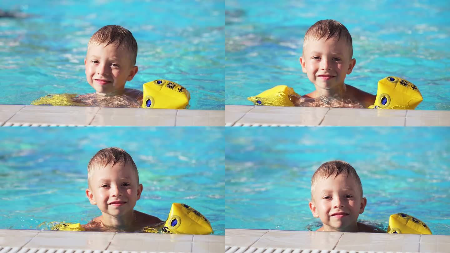 戴着臂章在游泳池里洗澡和游泳的白人男婴的脸部特写。孩子趴在泳池边看镜头。暑假的休闲活动。享受快乐的童