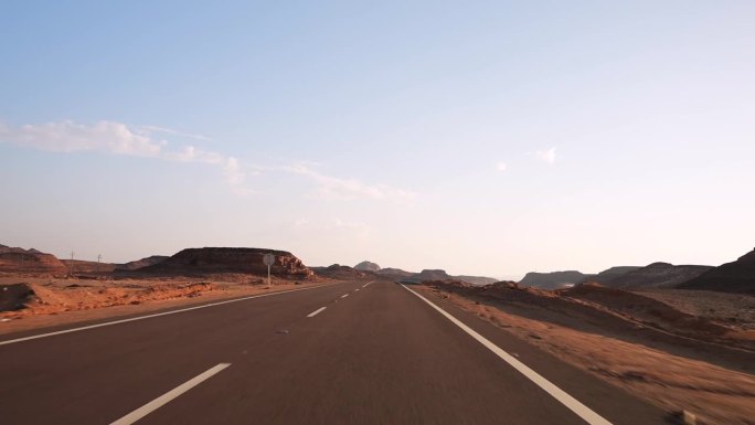 日落时分，沙漠中空旷的柏油路上行驶的快速汽车的正面视图，路面上有标线。路边的沙丘