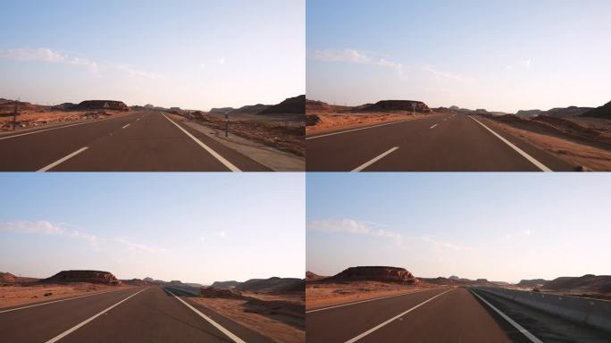 日落时分，沙漠中空旷的柏油路上行驶的快速汽车的正面视图，路面上有标线。路边的沙丘