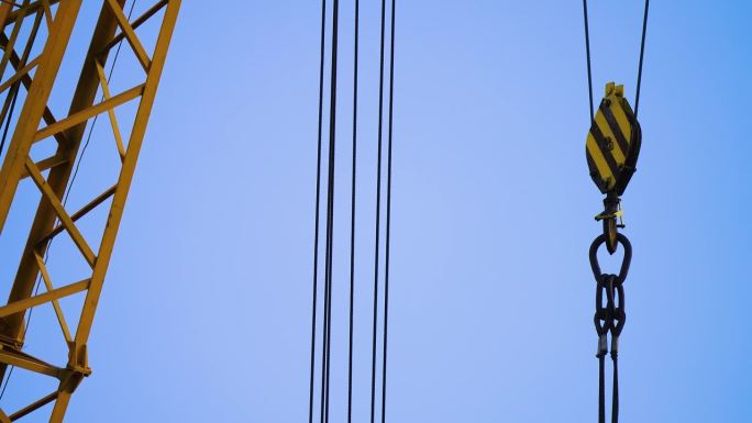 在蓝天的映衬下，钢索和钢钩挂在起重机坚固的吊杆上