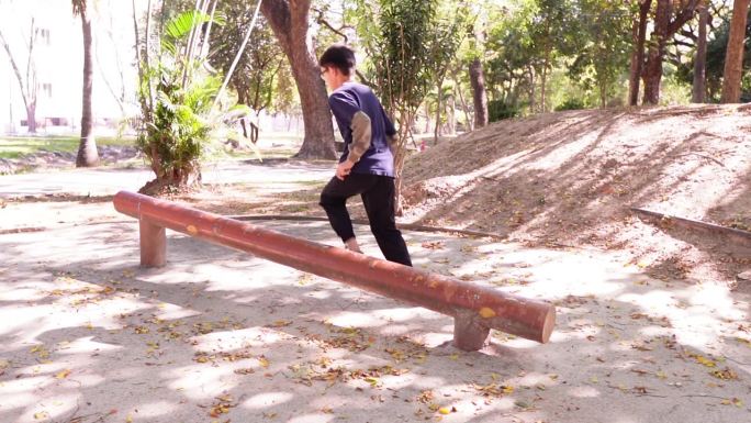 在一个公共健身公园里，一个小男孩展示了一项运动，他跳过一根木头来训练腿部和脚踝的肌肉。
