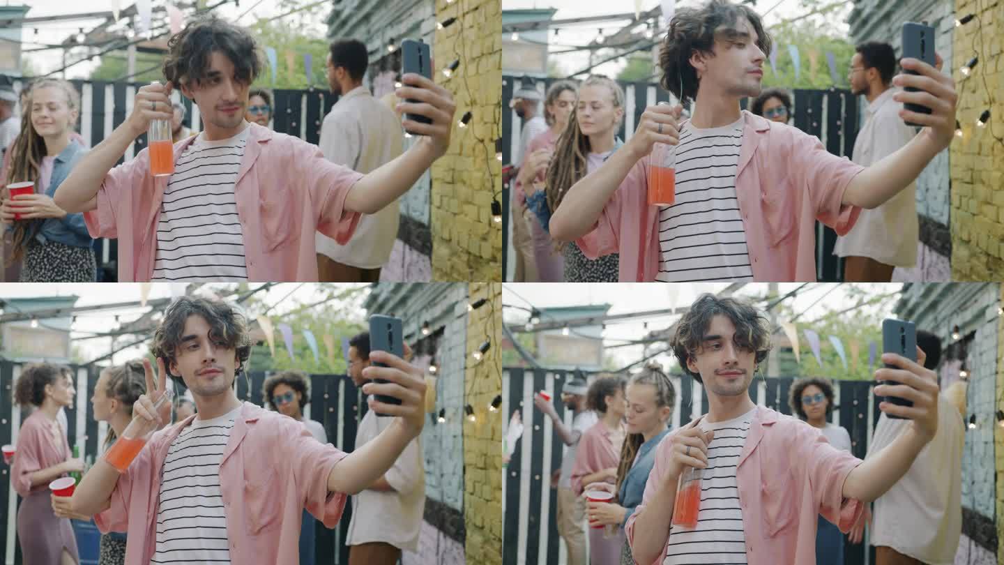 快乐的年轻人拿着一瓶饮料和朋友们在露天派对上对着智能手机拍照自拍