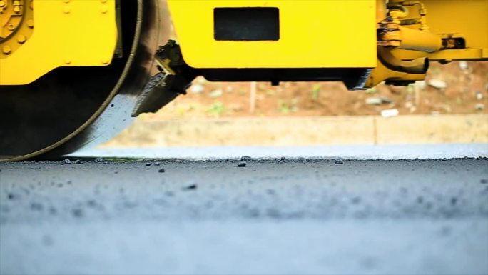 工人使用压路机压实沥青，串联式压路机是一种重型压实施工车辆，用于平整道路施工中的土壤，砾石，混凝土或