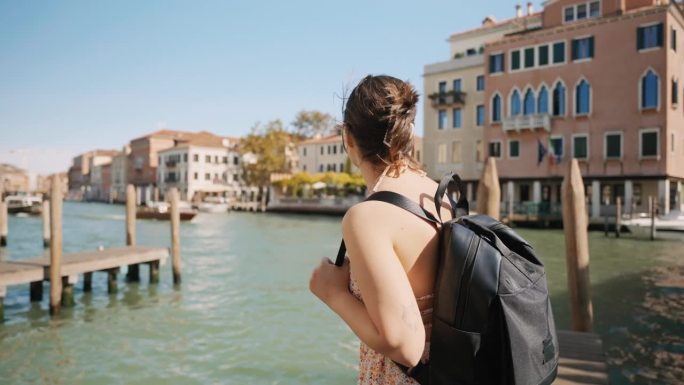 度假期间，威尼斯蓝天下的运河旁，背着背包微笑的年轻女游客