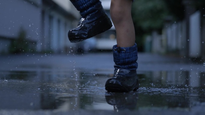 穿着雨靴的孩子在水坑上行进，溅起的水花在空中飞舞