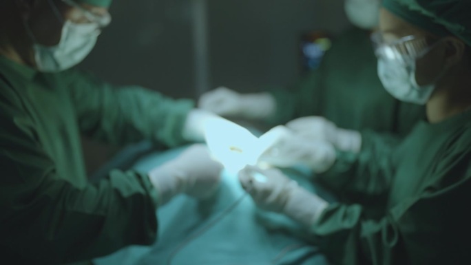 在医院的手术室里，当外科医生在病人的伤口上进行手术缝合时，手术团队顺利合作的模糊动作。