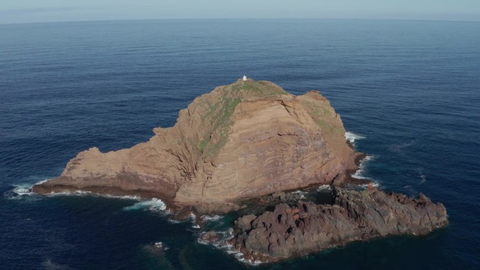 宁静的蓝绿色海洋中的巨石，上面有一座小灯塔。史诗级的无人机镜头放大倾斜。在葡萄牙马德拉岛的莫尼兹港。