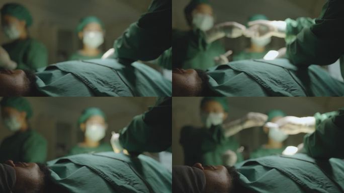 一名男性患者麻醉后躺在手术床上的特写，以及在低照度的手术室中，一名外科医生和他的团队在照明的手术灯下