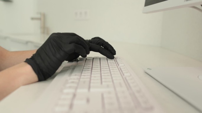 在诊所工作时，双手戴着黑色丁腈手套，使用键盘。医学概念。