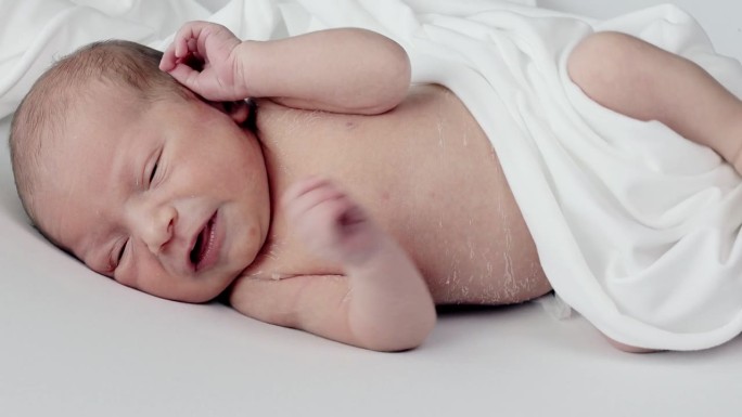 新生的婴儿在白色的被单上哭泣。幼稚的脾气。婴儿绞痛和腹痛。婴儿用的药物和维生素