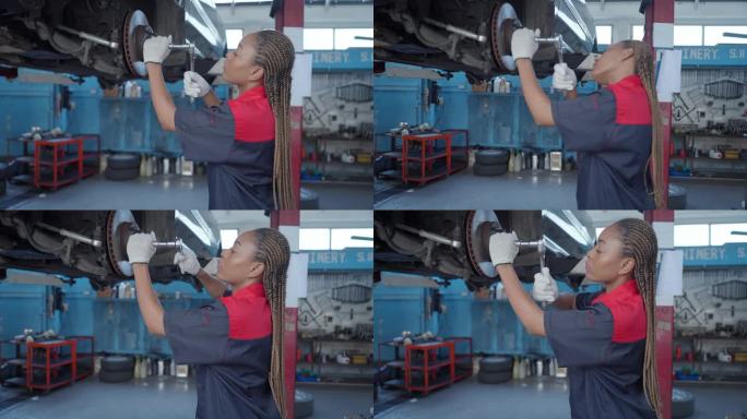 专业女汽车工程师在汽车修理厂用套筒扳手修理故障车辆的车轮部分。成年女工程师在车库里用工具修理汽车。