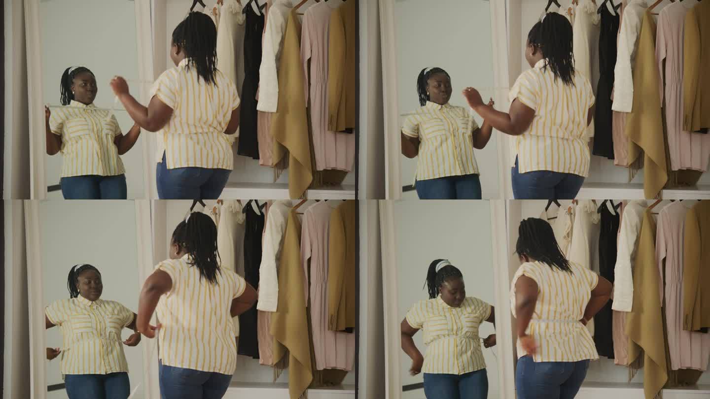 黑人女性减肥后在镜子前欣赏自己。快乐的非洲超重女性在家里跳舞。加码女性测量腰围。