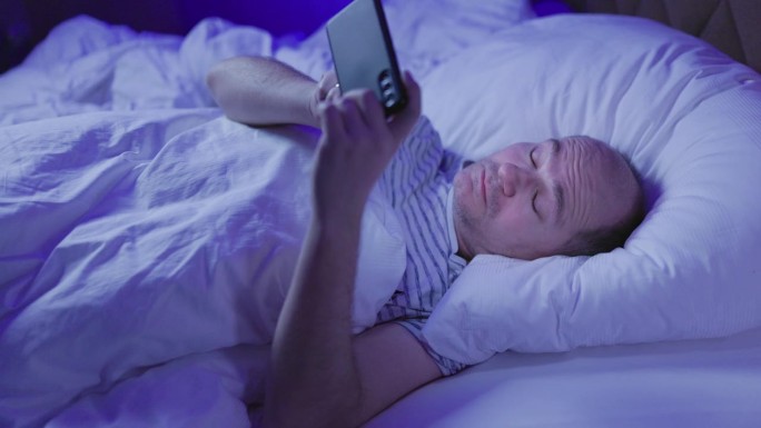 中年秃顶男子躺在床上玩手机