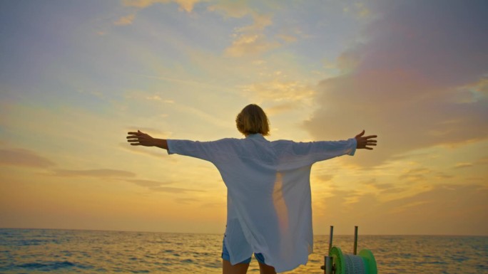 日落时分，克罗地亚多云的天空下，女游客站在帆船上，伸开双臂