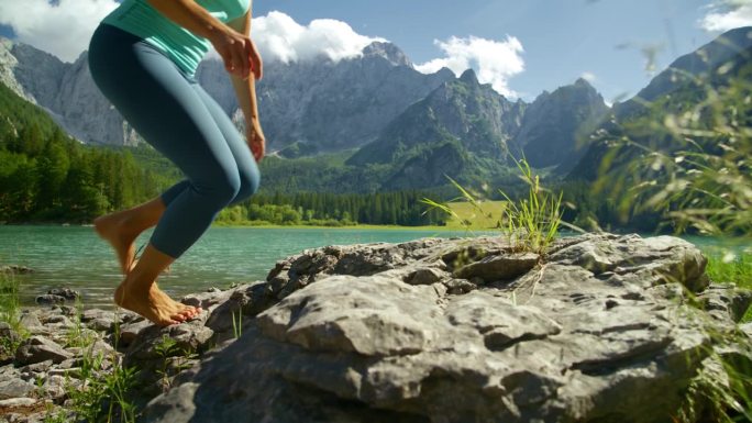赤脚女人沿着阳光明媚的山间湖泊踩在岩石上