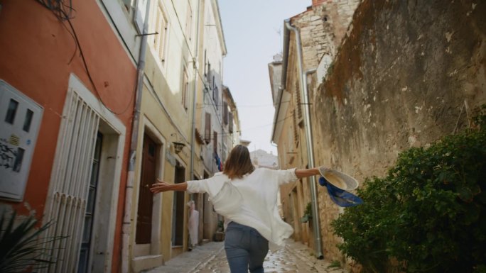 SLO MO微风般的幸福:在罗维尼的永恒小巷里，女人张开双臂快乐地奔跑。简单的动作变成了对自由和快乐