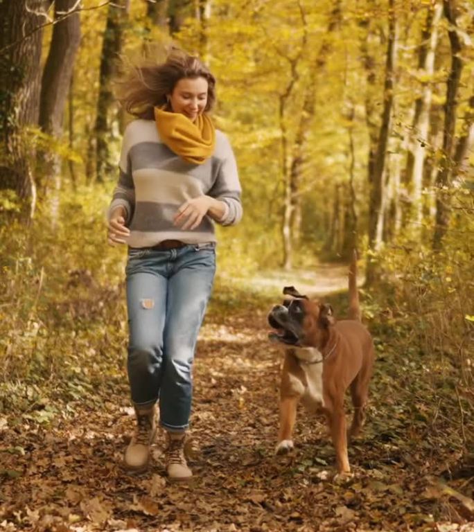 秋天里，快乐的年轻女子和爱犬在树林中奔跑