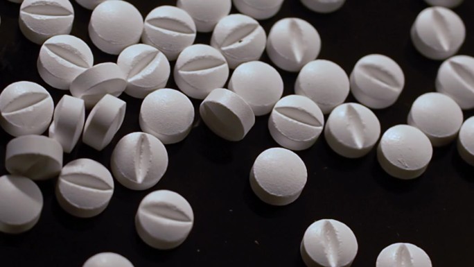 一堆白色药片散落在黑色表面，美国阿片类药物危机。