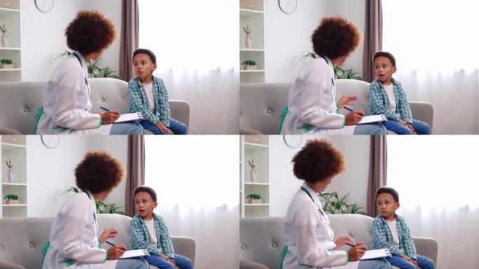 非裔美国儿科医生坐在沙发上，和一个学龄前的小男孩在家里体检时聊得很开心。好心的医生在膝盖上用写字板记