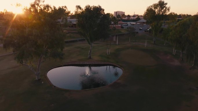 空中无人机拍摄的高尔夫球洞与喷泉和池塘在日出