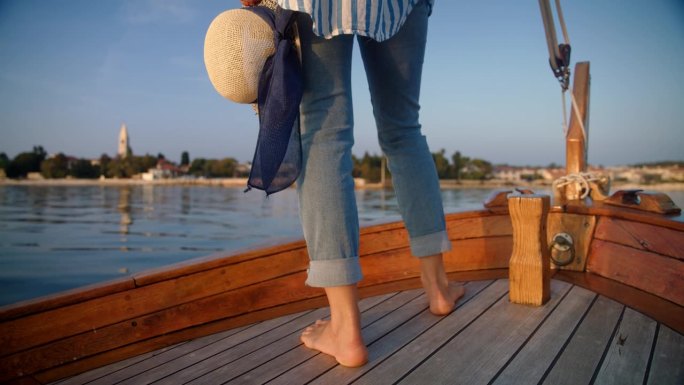 一个不知名的女人赤着脚站在船上，拿着一顶帽子，在黄昏时分驶向岛屿