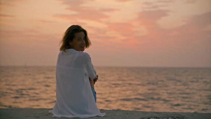 SLO MO海滨日落:一个女人安静地坐在码头上，欣赏着令人惊叹的海上日落