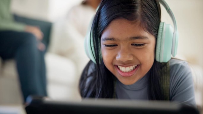 女孩，耳机和平板电脑，用于在线学习，视频通话和流媒体平台的在线教育。来自印度尼西亚的小孩在地板上听音