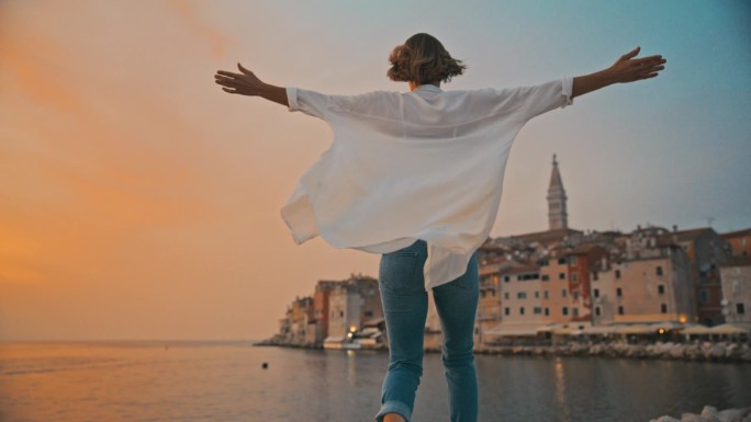 日落的幸福:一名女子在罗维尼的一个码头上奔跑，她张开双臂，幸福地表达着幸福