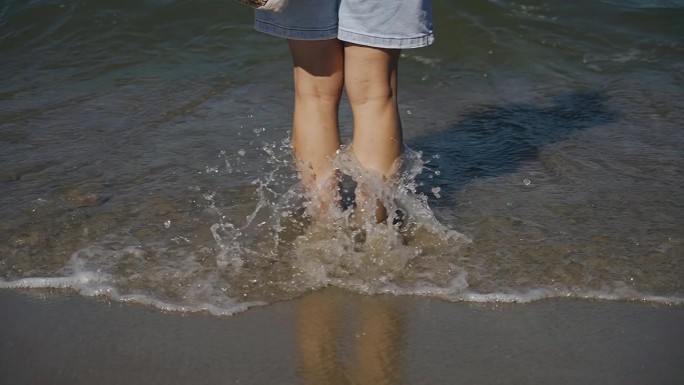 一个女人站在海边的沙滩上，海水洗着她的脚。慢动作画面