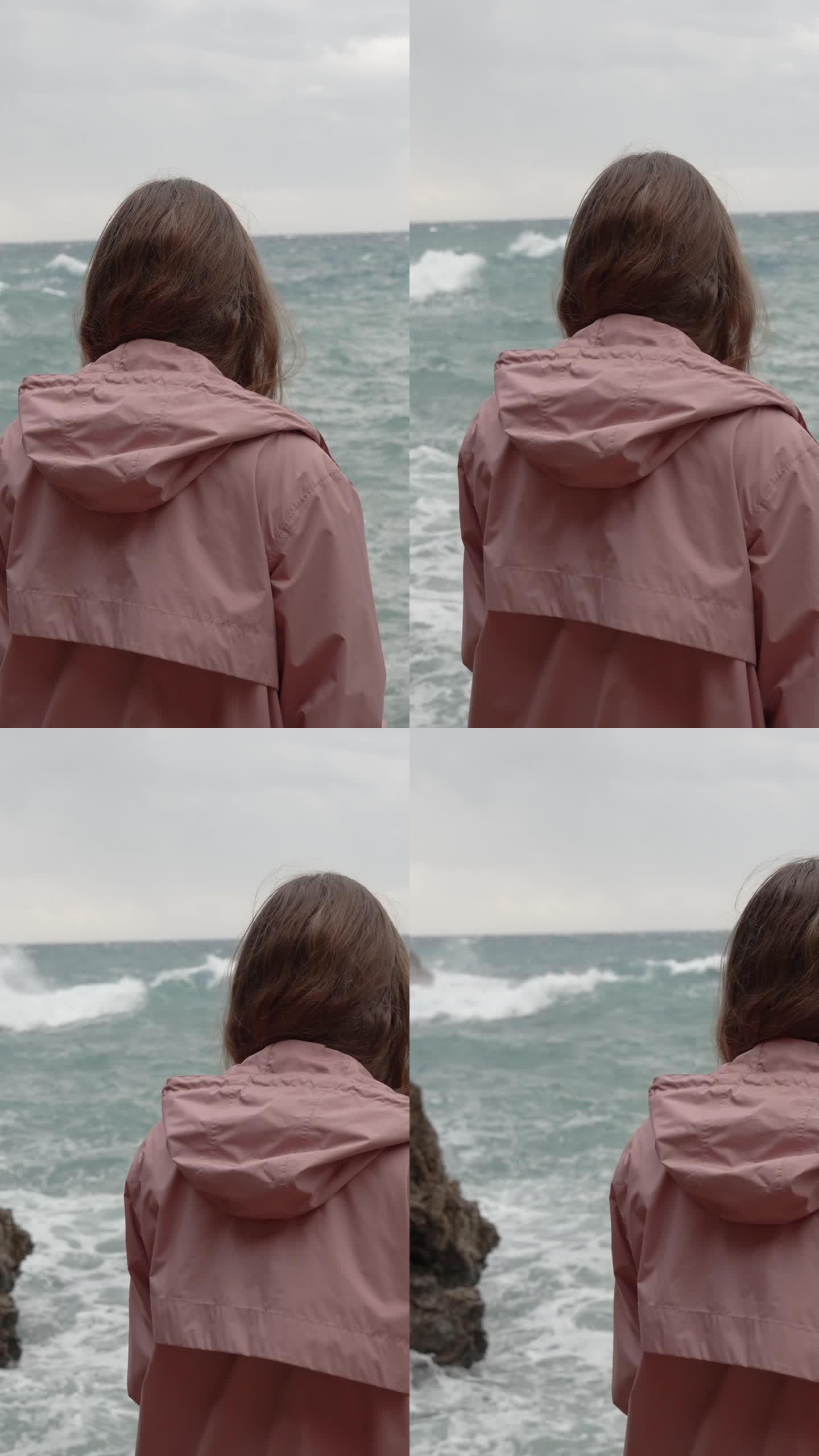 垂直视频。一个孤独的女人凝视着远处汹涌的大海，海浪冲击着尖锐的岩石。缓慢的运动。