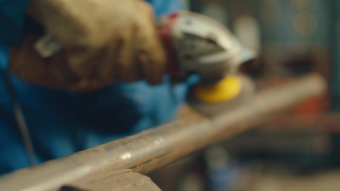 戴手套的铁匠用电动工具打磨钢管