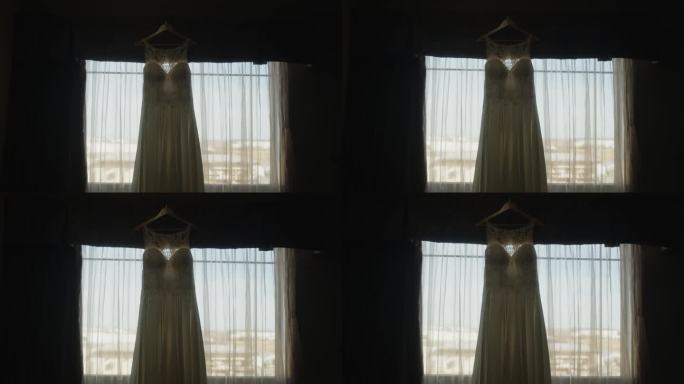美丽的白色婚纱挂在衣架上，背光窗帘，在电影的慢镜头中，喜怒无常的风景在移动。