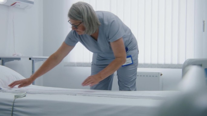 成熟的护士在病房里铺床，为病人准备床铺