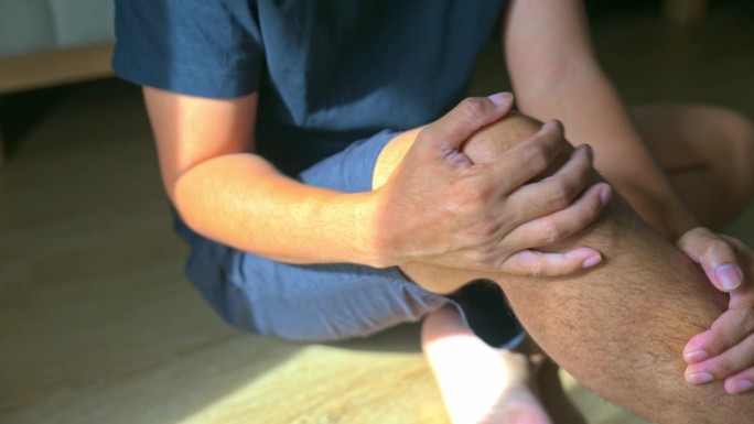 亚洲男子抱着膝盖疼痛。男患腿痛在家。医疗保健理念