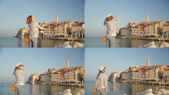 阳光时尚:一名女子戴上帽子，凝视着罗维尼的海岸美景
