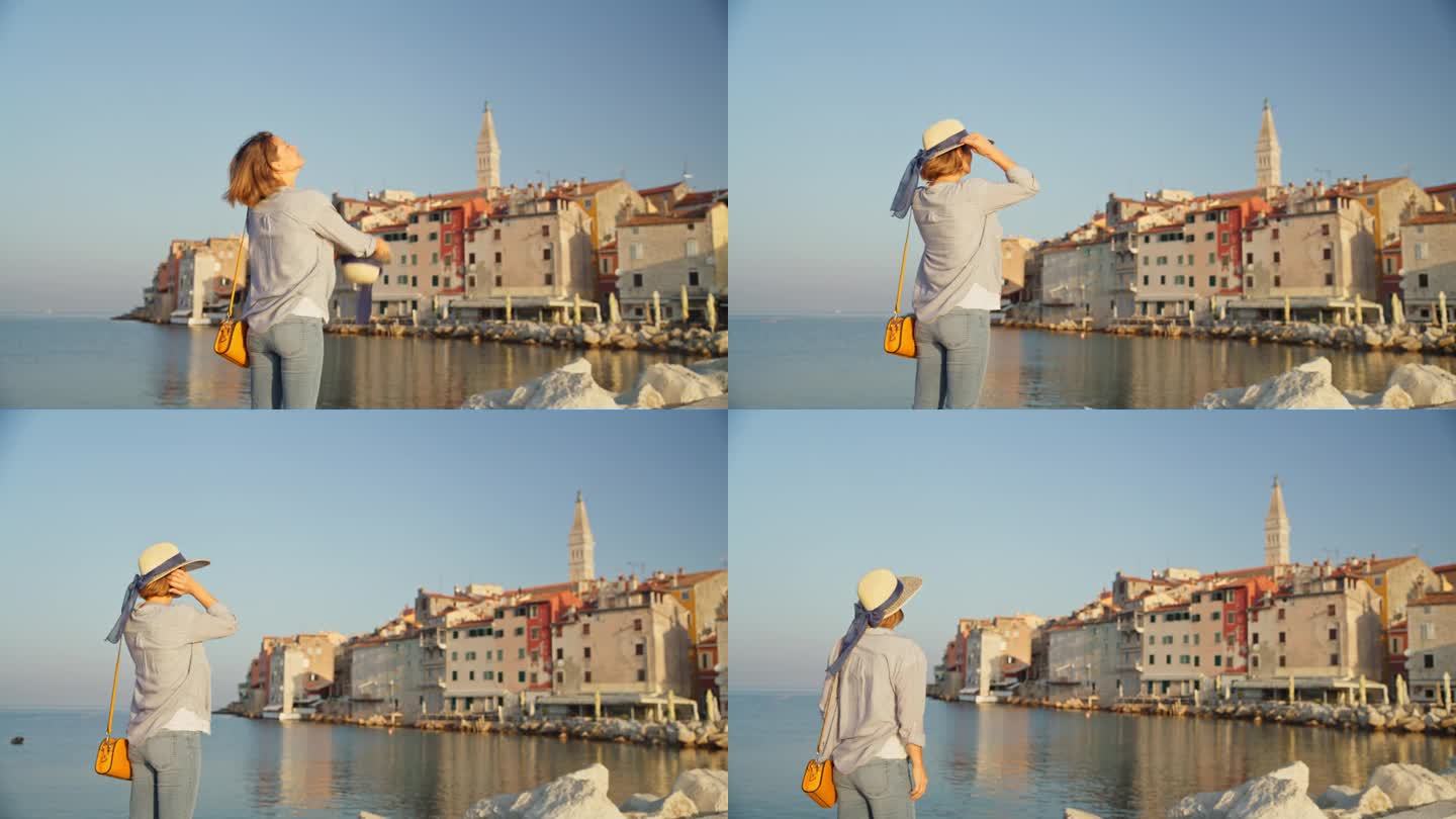 阳光时尚:一名女子戴上帽子，凝视着罗维尼的海岸美景