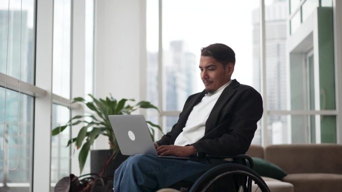 身体残疾的商人坐在轮椅上，在办公室使用笔记本电脑