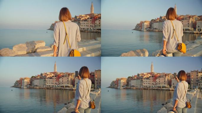 清晨漫步:女人在罗维尼日出的宁静美景中，在码头上用手机捕捉老城的魅力