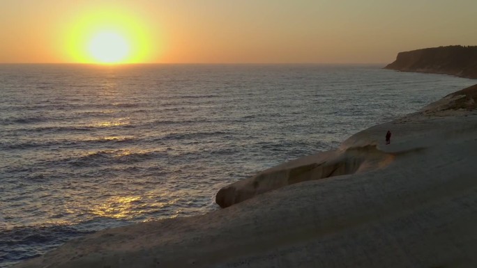 无人机拍摄的一对情侣在意大利撒丁岛苏留岛和萨伊德岛奇妙的地质构造中拥抱在一起，日落时太阳在地平线上