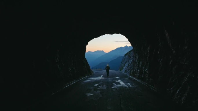 黎明时分，一个女人的剪影在黑暗的山间隧道里奔跑