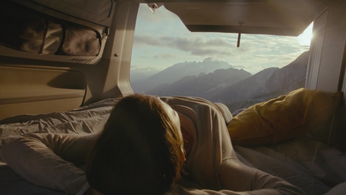 一名女子在面包车里放松，欣赏山景上的日出