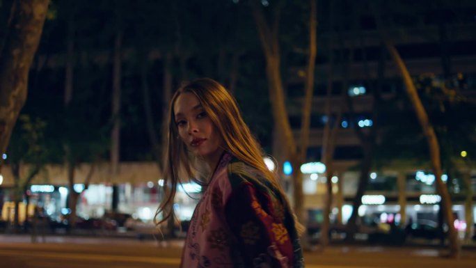 晚上在市中心散步的女人看着相机。女孩在深夜漫步城市