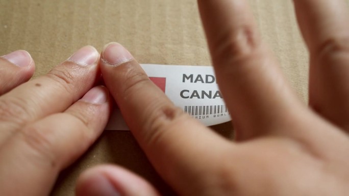 手应用在加拿大制造的旗帜标签上的运输箱与产品优质条码。制造和交付。产品出厂进出口。