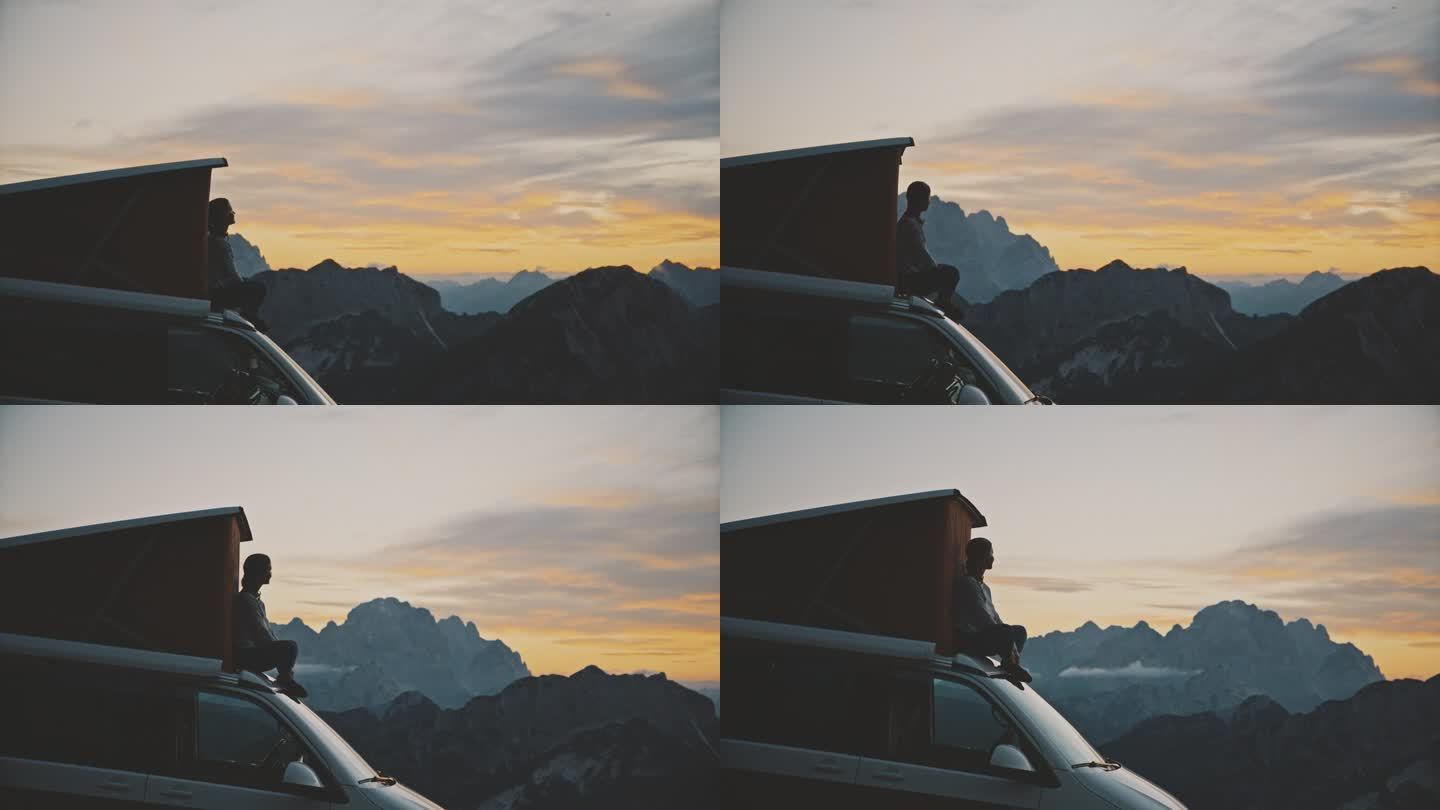 无忧无虑的女人在货车顶上欣赏山间的日出。一个女人欣赏美丽的山景。