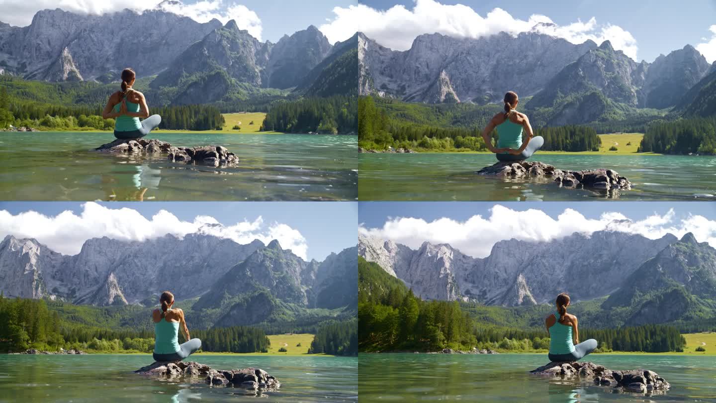 一个女人在阳光明媚、宁静的山间湖泊的岩石上沉思