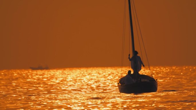 SLO MO剪影海岸奥德赛:女人站在船头，男人驾驶船进入日落的幸福